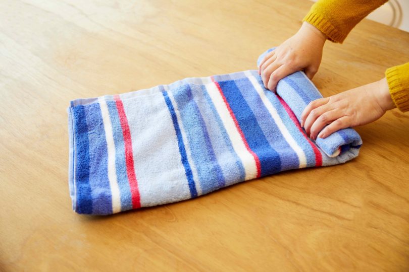 バスタオルの長辺を四つ折りにし、端からくるくる巻く。