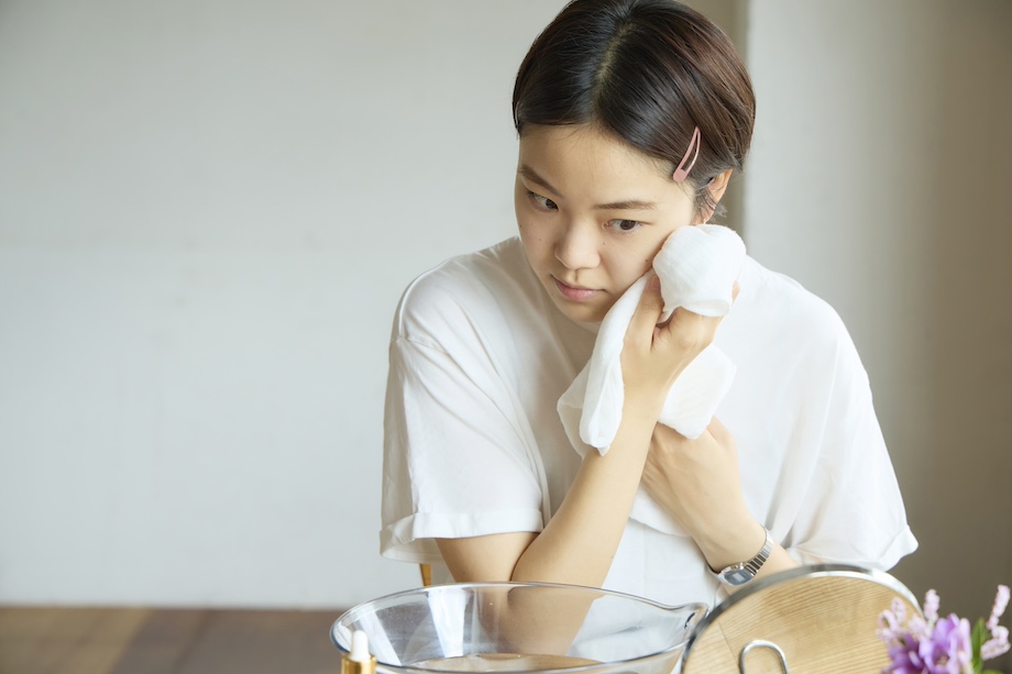 蒸しタオルで顔の汚れを拭う女性